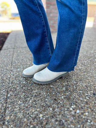 Person wearing dark wash cropped flare jeans with raw hem and light colored shoes on pavement