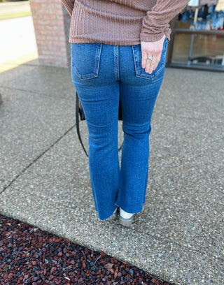 Woman wearing dark wash cropped flare jeans with raw hem and cable knit sweater from behind