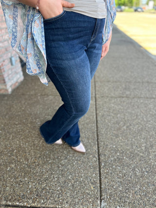 Woman wearing dark wash skinny bootcut jeans with floral cardigan standing on concrete sidewalk