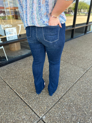 Woman wearing dark wash skinny bootcut jeans with floral top, standing on concrete sidewalk outdoors.