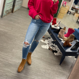 Person wearing light wash distressed crop skinny jeans with brown boots in boutique setting