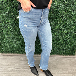 Woman wearing light wash distressed straight leg jeans with black boots against green hedge backdrop