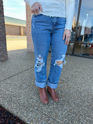 Person wearing distressed medium wash dad jeans with ripped knees and cuffed hems, paired with brown boots.