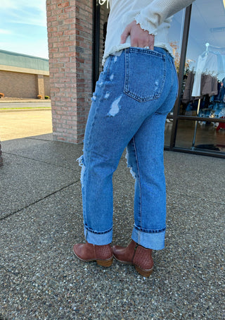 Person wearing distressed medium wash straight leg jeans with brown ankle boots, showing back view and styling details.