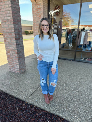 Woman wearing distressed medium wash jeans with brown boots standing outside clothing store.