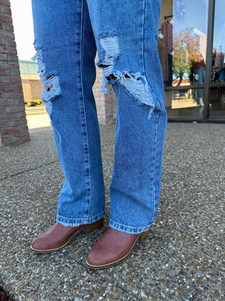 Person wearing distressed medium wash straight leg jeans with frayed holes and brown ankle boots.