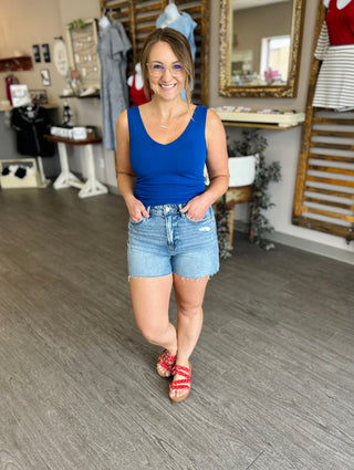 Woman wearing blue tank top and distressed denim shorts with raw hem in clothing store setting.