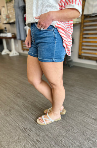 Woman wearing cuffed denim shorts with striped top and sandals, showing casual summer styling.