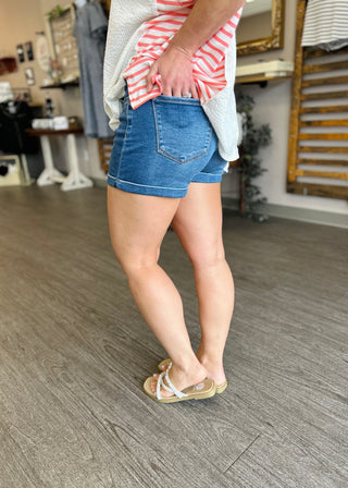 Woman wearing high-rise cuffed denim shorts with striped top and sandals in casual indoor setting.