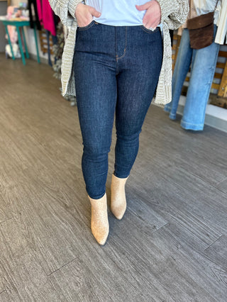 Woman wearing high-waisted skinny jeans with embroidered pocket detail and ankle boots in boutique setting.