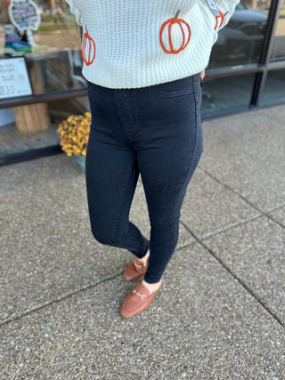 Woman wearing high-waisted black pull-on skinny jeans with white pumpkin sweater and orange shoes