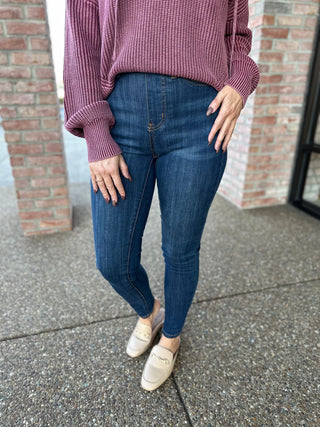 Woman wearing dark wash high-waisted pull-on skinny jeans with purple sweater and beige loafers.