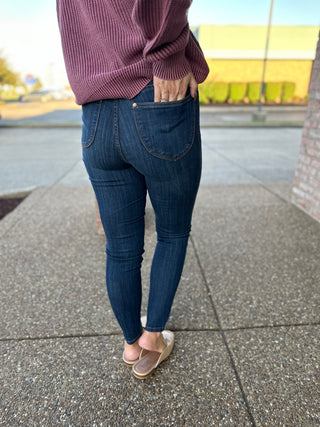 Woman wearing dark wash high-waisted pull-on skinny jeans with purple sweater and nude flats on sidewalk