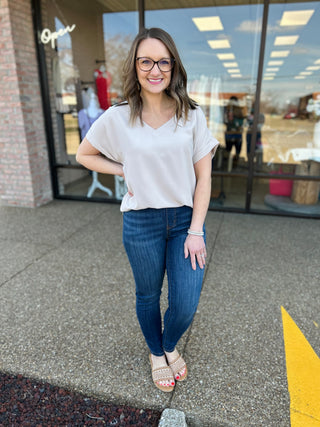Woman wearing light gray v-neck top and dark wash skinny jeans standing outside boutique storefront.