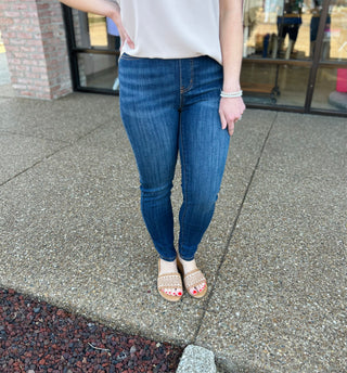 Woman wearing dark wash high-waisted pull-on skinny jeans with white top and sandals