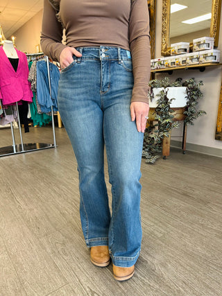 Person wearing high-waisted tummy control petite flare jeans with brown sweater and tan boots in clothing store.