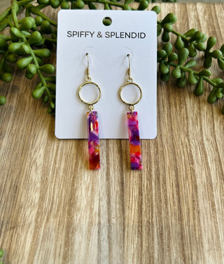 Colorful watercolor resin bar earrings with gold circles on branded card with green foliage background