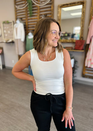 Woman wearing ivory square neck tank top with black pants, smiling in casual boutique setting.