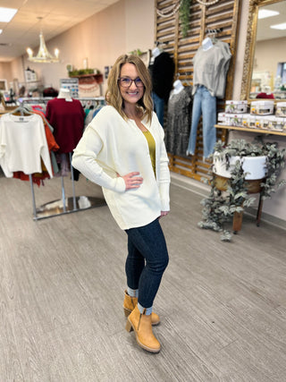 Woman wearing ivory ribbed front-clasp cardigan with jeans and boots in clothing boutique setting