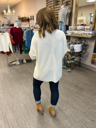 Woman wearing ivory ribbed front-clasp cardigan with jeans and boots in clothing boutique store
