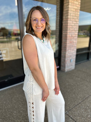 Woman wearing a sleeveless linen top with floral lace side panels, paired with matching pants.