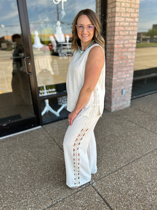 Woman wearing an ivory sleeveless linen top with lace detail pants outside a boutique.