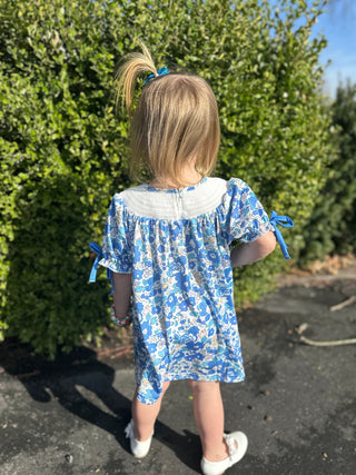 Young girl wearing blue floral dress with bow tie sleeves walking outdoors on sunny day