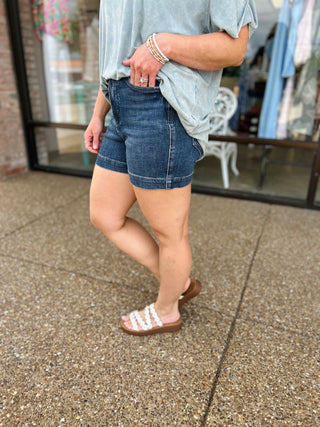 Woman wearing high-waisted denim shorts with double button detail, styled with striped top and sandals.