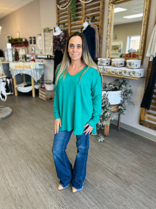 Woman wearing Kelly Green V Neck Sweater Top with jeans in retail boutique setting