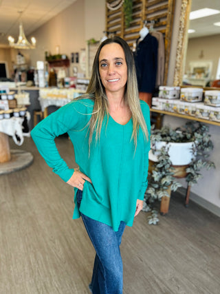 Woman wearing Kelly Green V Neck Sweater Top by Zenana in casual retail store setting