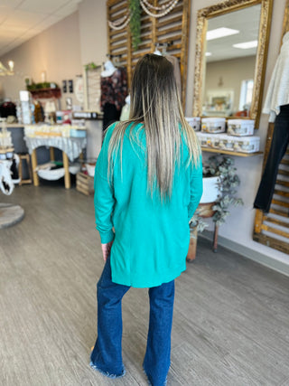 Woman wearing oversized green v-neck sweater with jeans in boutique setting, shown from behind