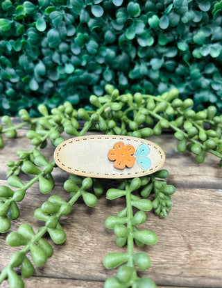 Handmade kids hair clip with flower design on wooden surface surrounded by green foliage