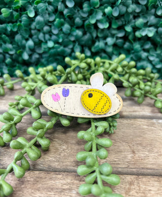 Handmade kids hair clip with bee design featuring yellow and white felt on wooden surface with green plants