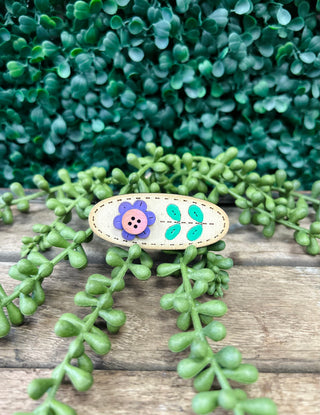 Handmade kids hair clip with flower and leaf design on wooden surface with green plants