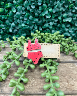 Handmade kids hair clip with decorative design on wooden surface surrounded by green succulent plants