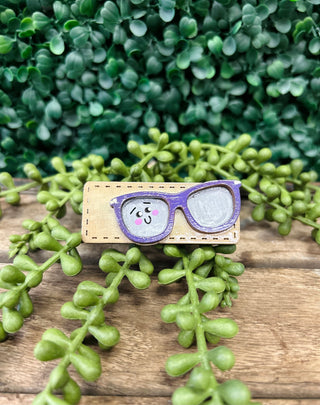 Handmade kids hair clip with cute eyeglasses design on wooden surface with green plants