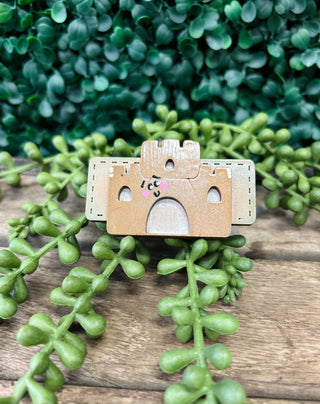 Wooden camera-shaped hair clip with cute face design displayed on rustic wood with green succulent plants