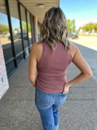 Woman wearing ribbed knit tank top with jeans, walking along covered walkway outdoors