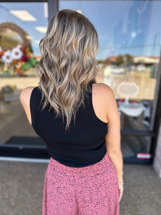 Woman wearing black knit ribbed tank top from behind, showing the sleeveless design and fitted silhouette.