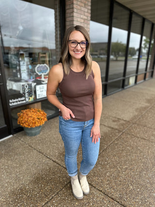 Woman wearing brown ribbed knit tank top with jeans and boots standing outside storefront