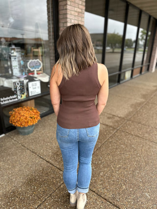 Woman wearing brown ribbed knit tank top and jeans, standing outside storefront showing back view.