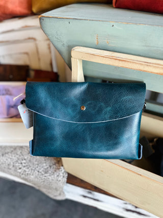 Large leather envelope crossbody bag with adjustable strap displayed on rustic wooden chair