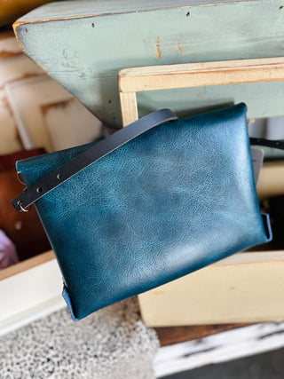 Large leather envelope crossbody bag with adjustable strap displayed on rustic wooden chair