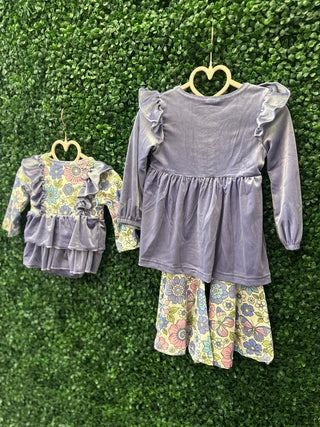 Two matching girls' outfits with lavender velvet tops and floral print bottoms hanging on heart-shaped hangers.