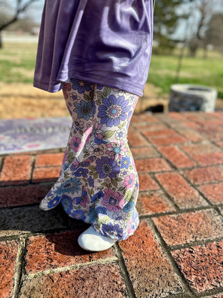 Child wearing purple top and floral print leggings standing on brick patio outdoors