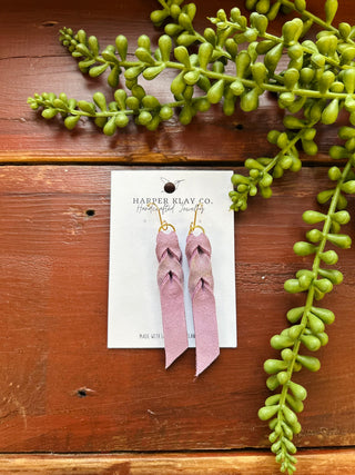 Pink leather earrings on Harper Klay Co. jewelry card surrounded by green succulent plants on wooden surface.