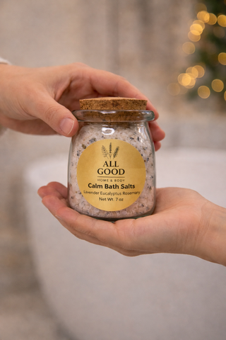 Hands holding a glass jar of All Good Home & Body Calm Bath Salts with cork lid.