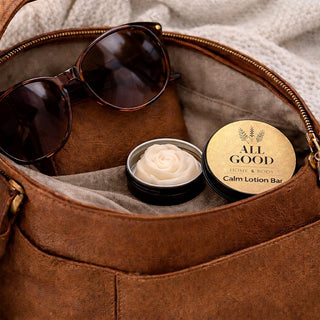 All Good Home & Body Calm Lotion Bar in open tin inside a leather bag with sunglasses.