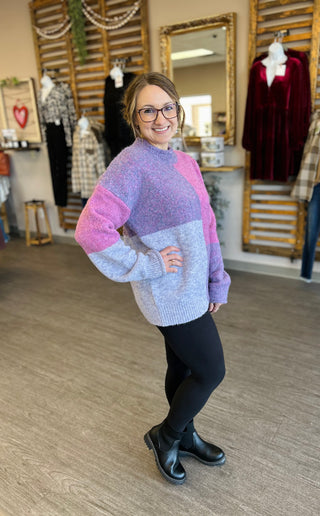 Woman wearing colorblock sweater in boutique store with clothing displays and wooden fixtures in background.