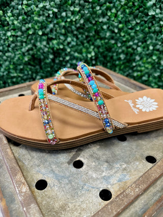 Colorful beaded sandals with rhinestone straps and brown soles displayed on wooden surface